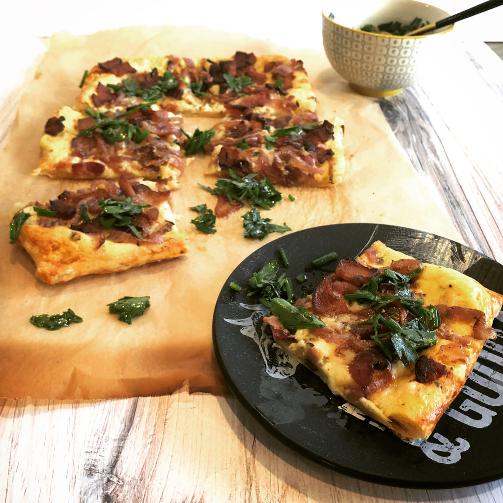 Bacon and Red Onion Tart on a black plate and wood cutting board
