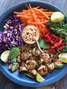 Chicken Meatballs with Peanut Sauce served on a platter with thinly sliced carrots, purple cabbage and arugula